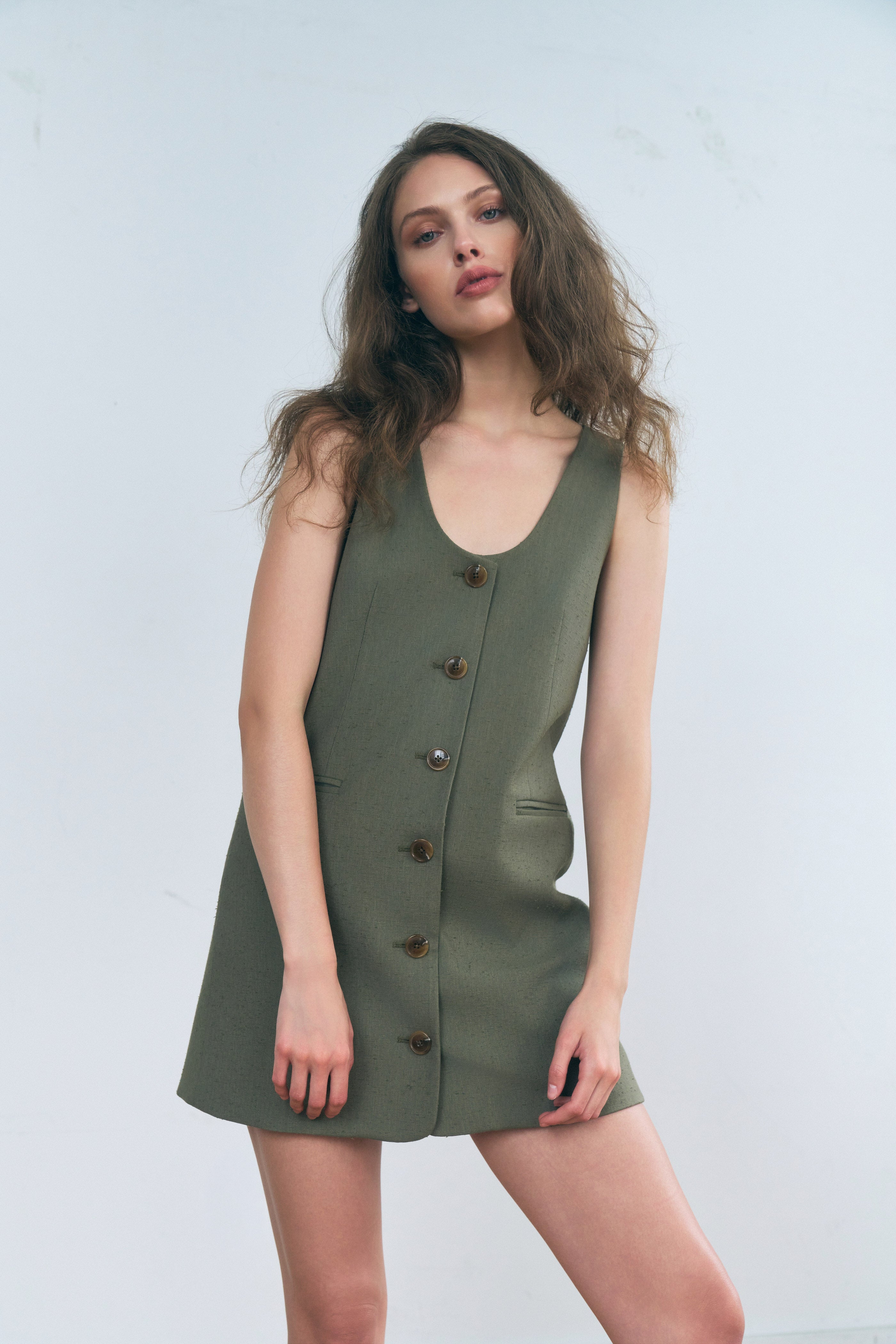 Malva dress in Smoked Olive — Premium Japanese Nep Textured Fabric, sleeveless silhouette, low U-shaped neckline, double welt pockets, front button closure, half-body front alternate
