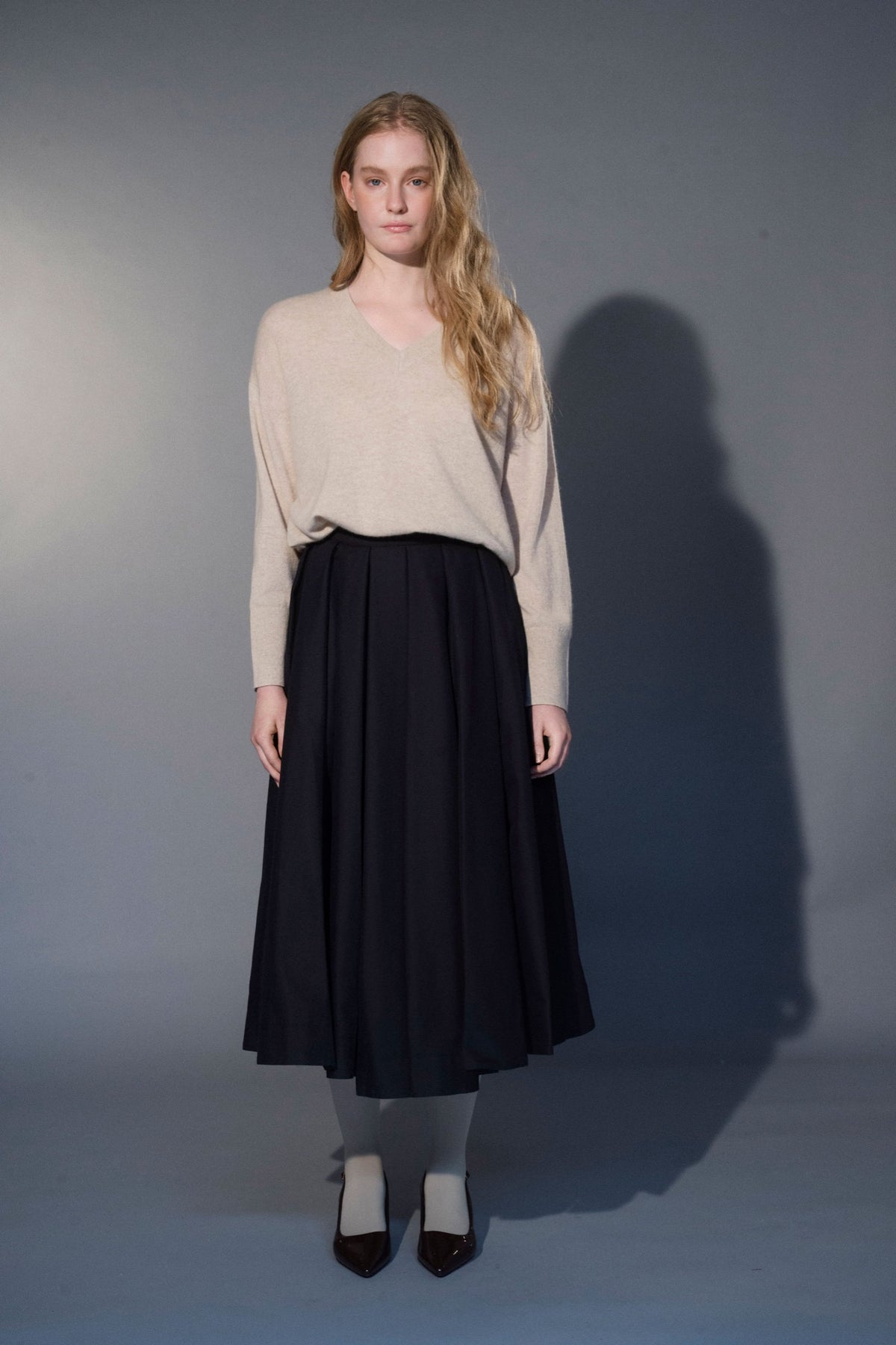 Woman wearing the Stathe Vinorama Skirt in Black with the Salvia V-neck Sweater — editorial
